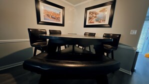 Zona pranzo con tavolo rotondo e sei sedie, quadri alle pareti e una ventola a soffitto.