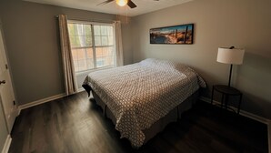 Una camera da letto con un letto, una ventola a soffitto, una finestra, un quadro e una lampada da terra.