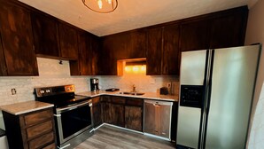 Una cucina compatta con mobili in legno scuro, elettrodomestici in acciaio inossidabile e un backsplash in piastrelle bianche.