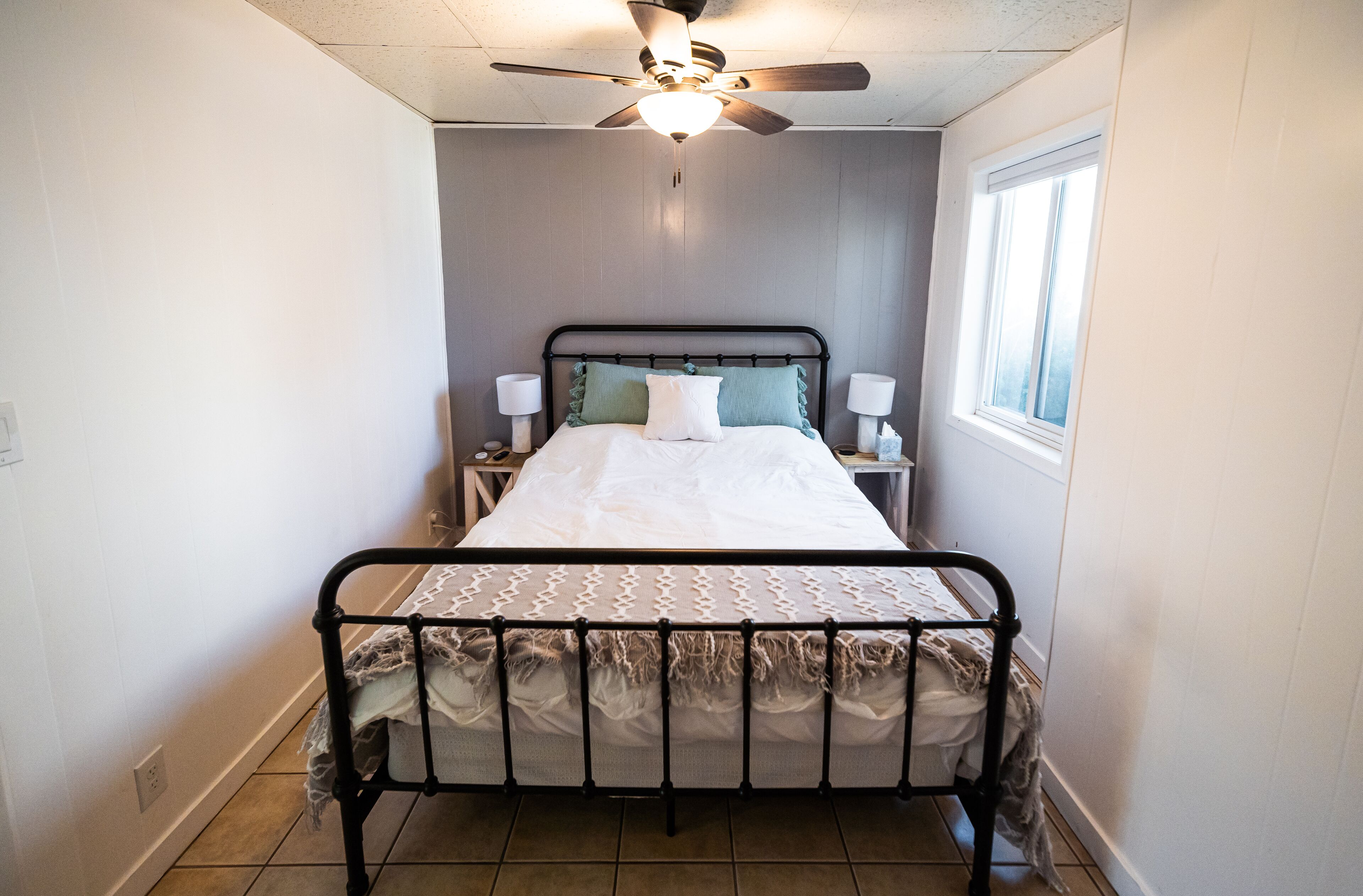A bedroom with a bed, two bedside tables, a ceiling fan, and a window.