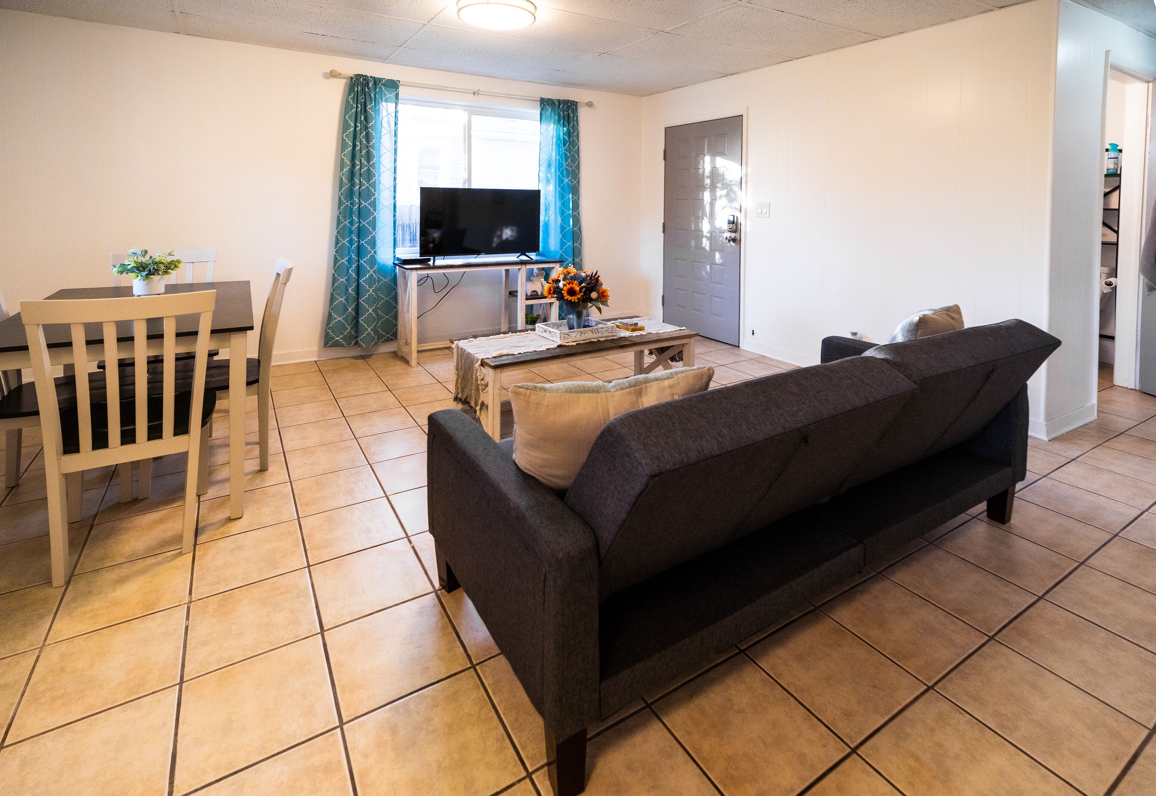 A living room with a sofa, a dining table, chairs, a TV, and a small table with flowers.