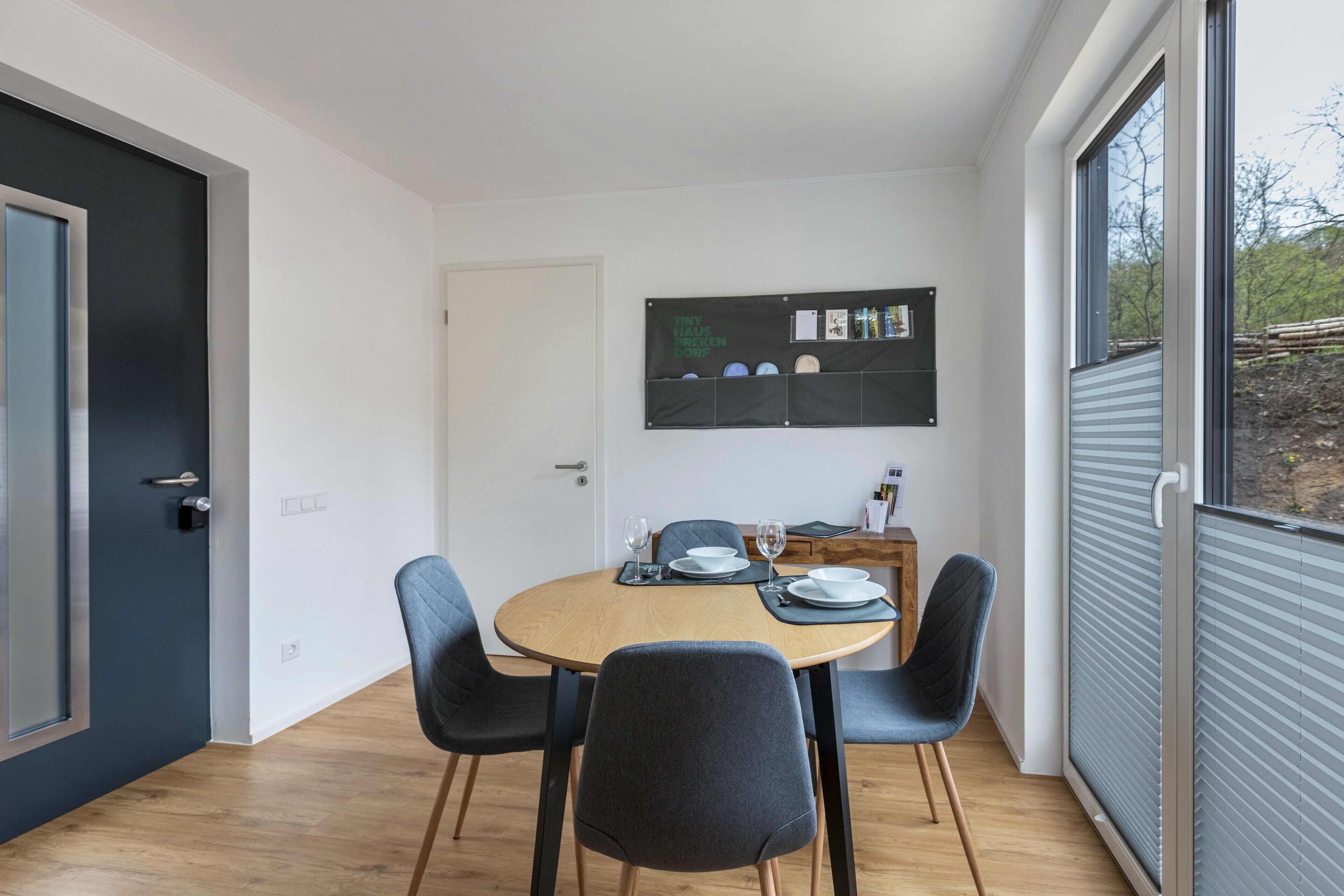 Ein Essbereich mit einem runden Tisch, vier Stühlen, einer Tafel mit Aufzeichnungen und einem Fenster mit Jalousien.