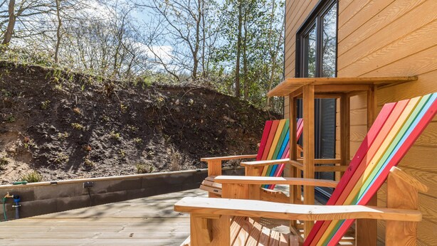 Una terraza de madera con sillas Adirondack, un edificio de madera y una ladera.