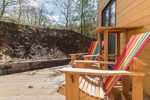 Una terraza de madera con sillas Adirondack, un edificio de madera y una ladera.