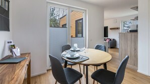 Un comedor moderno con una mesa redonda, cuatro sillas y vistas a un edificio cercano a través de amplios ventanales.