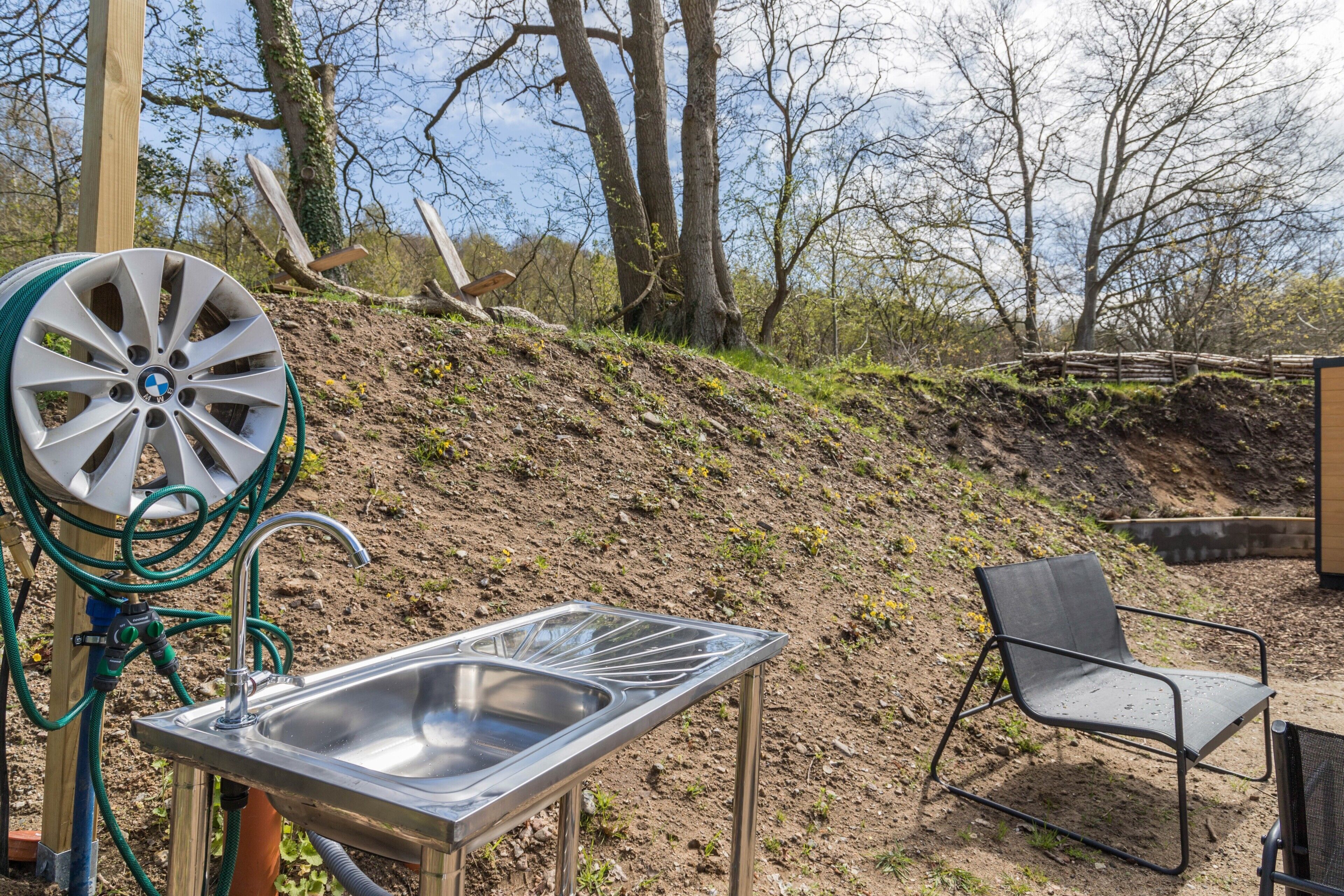 A metal sink with a hose, a chair, and a wooden post in a natural setting.