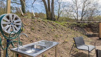 A metal sink with a hose, a chair, and a wooden post in a natural setting.