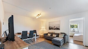 A modern living room with a dining area, a sofa, a TV, and a lamp. - Apartment 'Koje 1' with Private Terrace and Private Garden (Fehmarn)