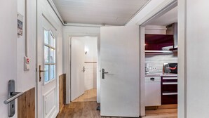 A hallway with a wooden floor, a white door, and a kitchen area with a dishwasher and cabinets. - Apartment 'Koje 1' with Private Terrace and Private Garden (Fehmarn)