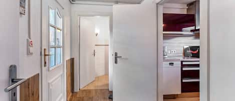 A hallway with a wooden floor, a white door, and a kitchen area with a dishwasher and cabinets.