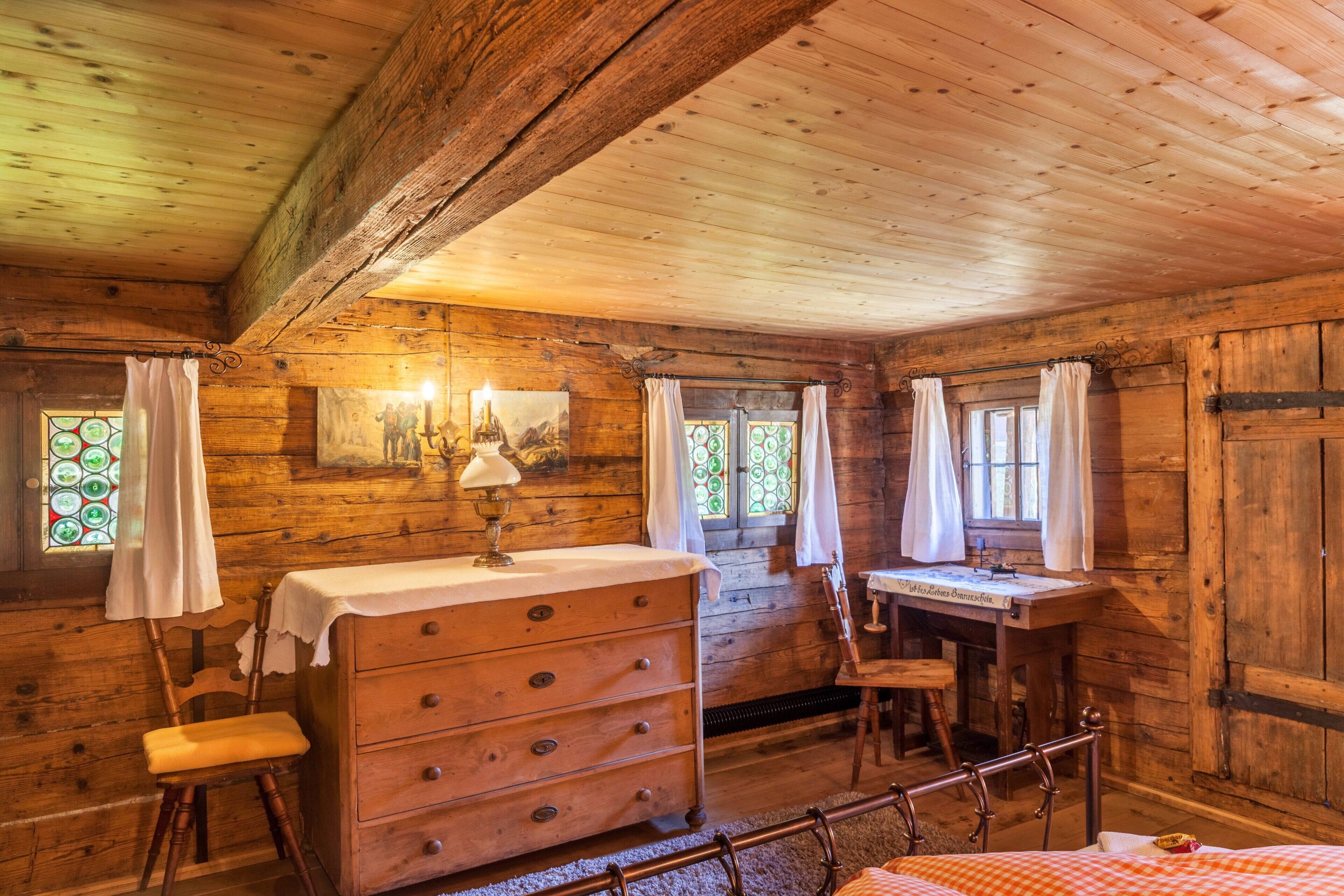 Une chambre dans un chalet en bois, comprenant un lit, une commode, une chaise et un bureau avec une lampe.