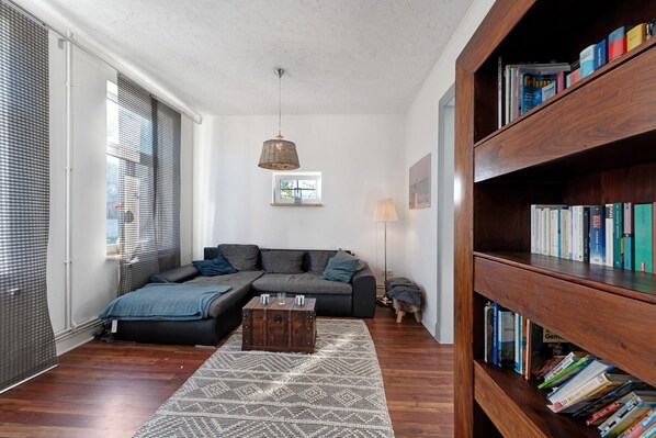 A modern living room with a sectional sofa, a wooden coffee table, a bookshelf, and a patterned rug.
