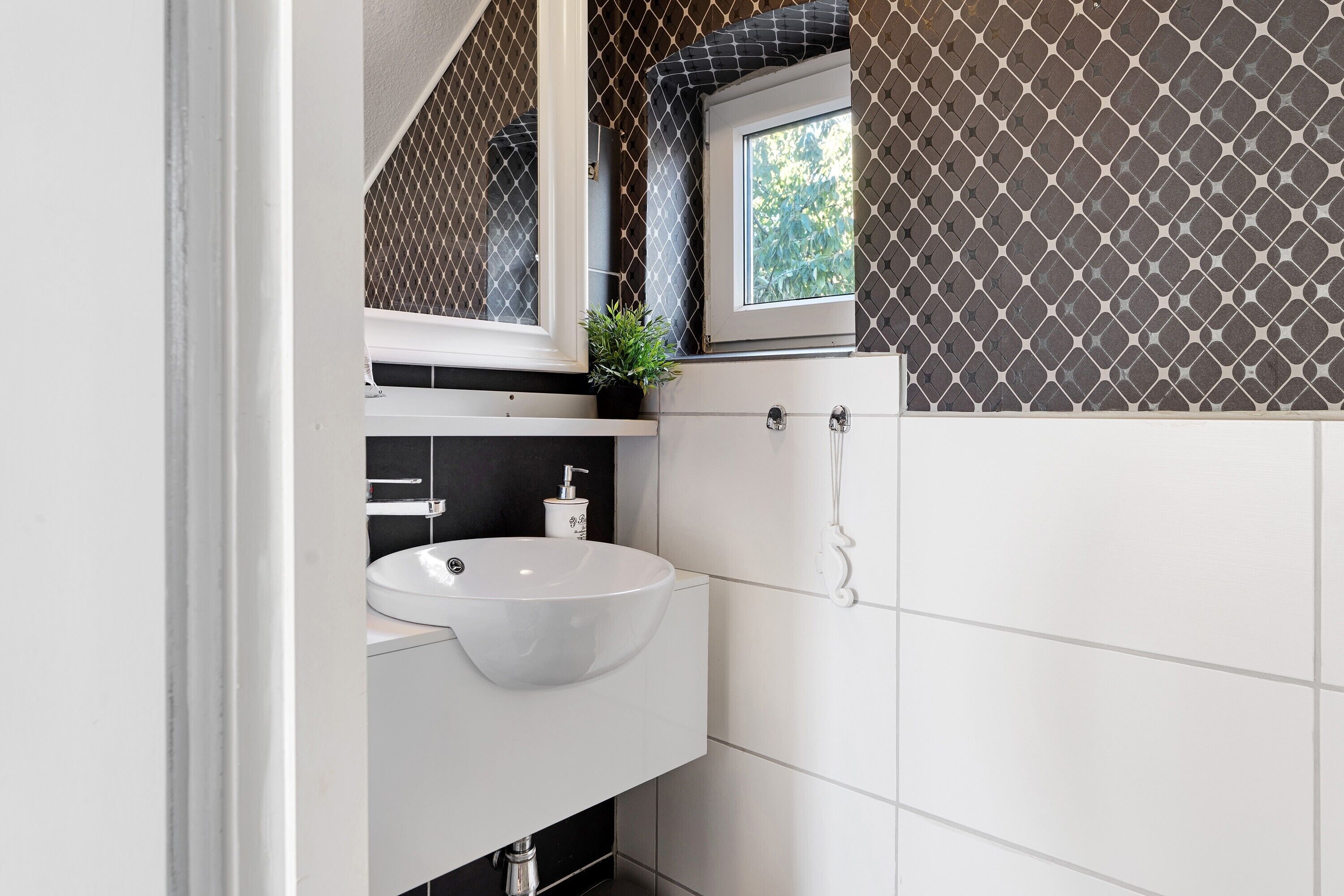 A bathroom with a white sink, a mirror, a window, and patterned tiles.
