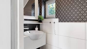 A bathroom with a white sink, a mirror, a window, and patterned tiles.