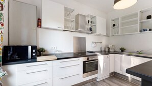 A modern kitchen with white cabinetry, a built-in oven, a microwave, and a sink. - Vacation Home "Insel Hus" with Private Terrace, Garden & Wi-Fi (Fehmarn)