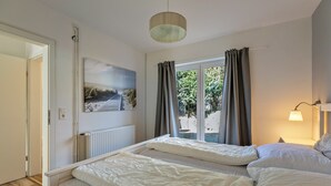 A room with two beds, a painting, a window with curtains, and a lamp. - Vacation Home "Deich Hus" with Private Terrace, Garden & Wi-Fi (Büsumer Deichhausen)