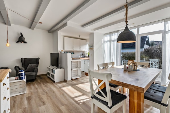 Una cocina moderna con armarios blancos, un comedor con mesa y sillas de madera, y un amplio ventanal que ofrece vistas al exterior.