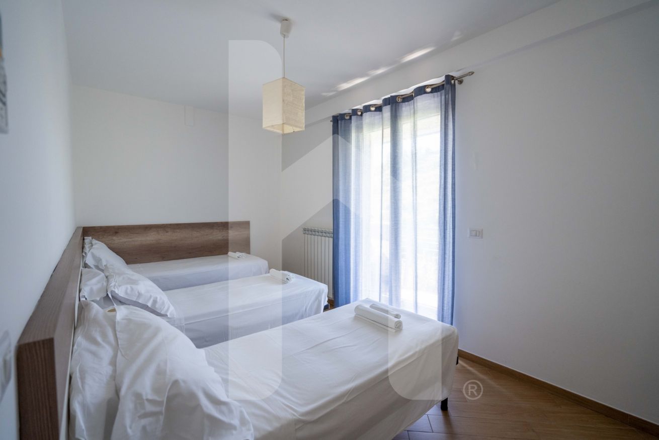 Una camera d'albergo con una struttura letto in legno, due letti singoli, un pavimento in legno, una finestra con tende blu e un lampadario.