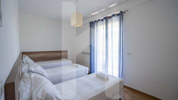 Una camera d'albergo con una struttura letto in legno, due letti singoli, un pavimento in legno, una finestra con tende blu e un lampadario.