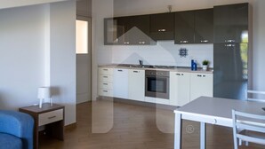Une cuisine moderne avec des armoires blanches, un four encastré et un réfrigérateur. On aperçoit une petite table et une chaise au premier plan.