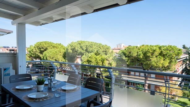 Un coin repas avec une table dressée pour quatre personnes, offrant une vue panoramique sur les arbres et les bâtiments.