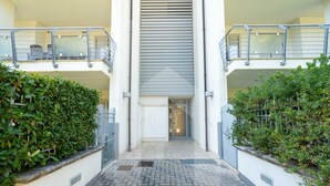 Un edificio moderno con una entrada central, dos balcones con barandillas y un camino de ladrillo que lleva a la entrada.