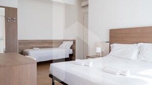 Una habitación de hotel con dos camas, cabecero de madera, una mesita de noche con lámpara y un armario.