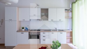 A modern kitchen with white cabinetry, a central island, and a dining table with a plant and a bowl of red flowers. - Kurioso - Three-room apartment ground floor with garden (Pineto)
