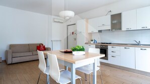 A modern kitchen with white cabinets, a wooden dining table, and a red handbag on a sofa. - Kurioso - Three-room apartment ground floor with garden (Pineto)