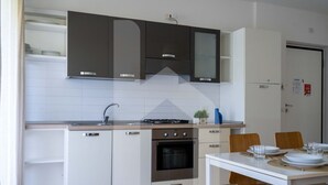 Una cocina compacta con armarios blancos, horno empotrado y comedor con mesa y sillas blancas.