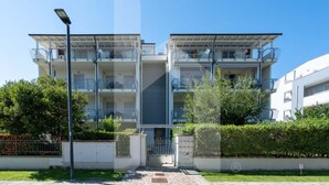 Un edificio de apartamentos moderno con varios balcones, una escalera central y una entrada con portón.