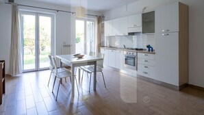 Une cuisine moderne avec des meubles blancs, une table à manger avec des chaises et une porte-fenêtre coulissante donnant sur un jardin.