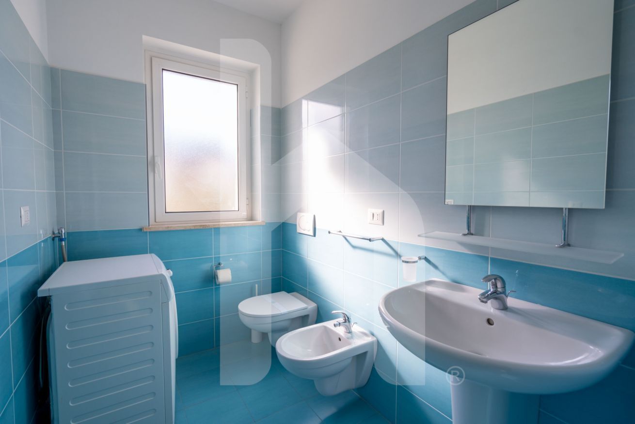 Une salle de bain avec des carreaux bleus, une fenêtre, des toilettes, un bidet, un lavabo et un porte-serviettes.