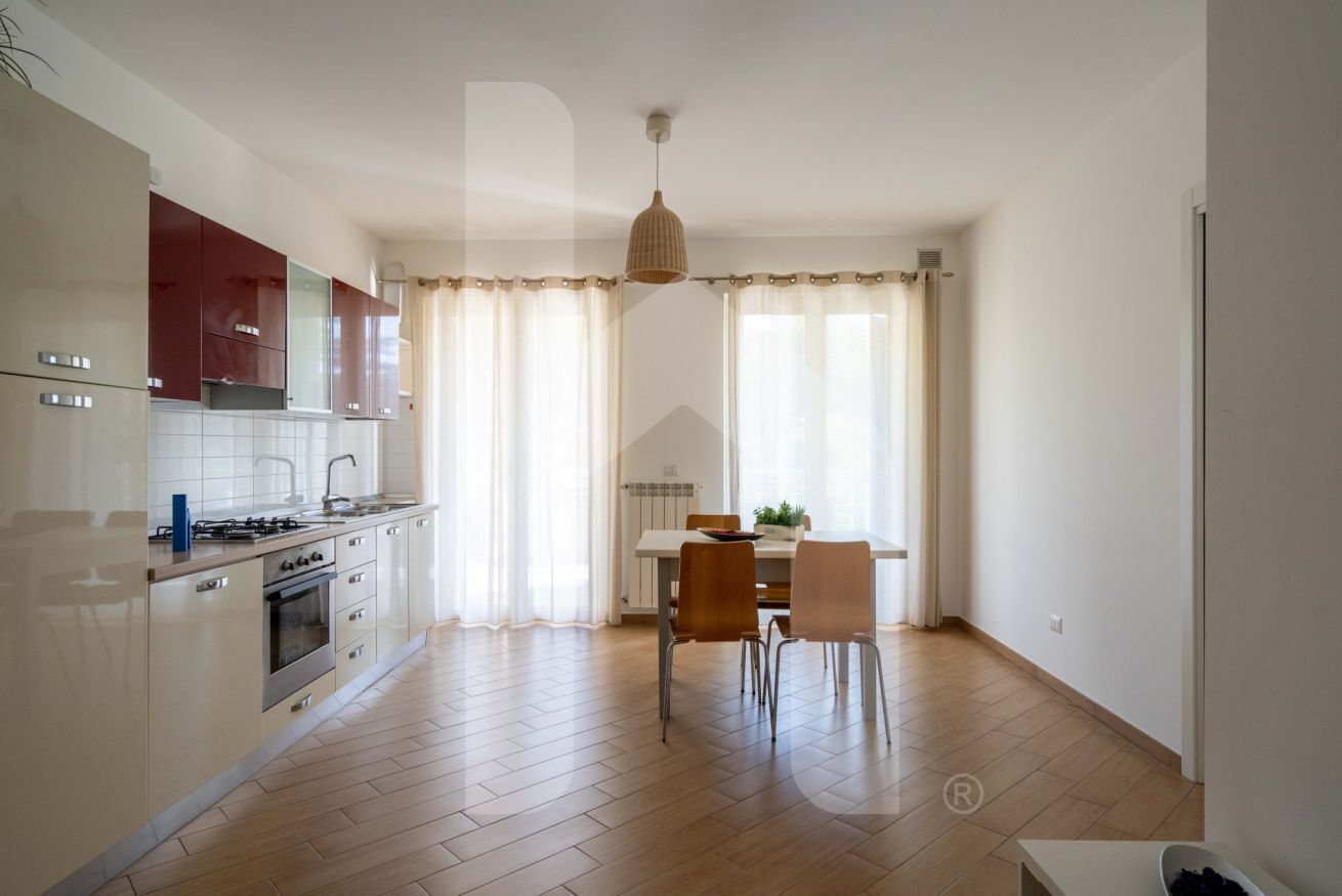 A modern kitchen with a dining area, wooden flooring, and a pendant light.