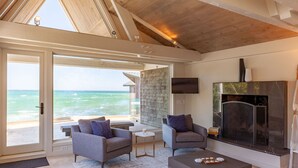 A spacious living room with a large sliding glass door leading to a balcony with a view of the ocean. There is a fireplace and a television mounted on the wall.