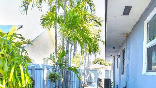 A covered patio with a round table and chairs, surrounded by palm trees and a white fence. - Miami Boho Beach Place - Great location for all your needs! (Hialeah)