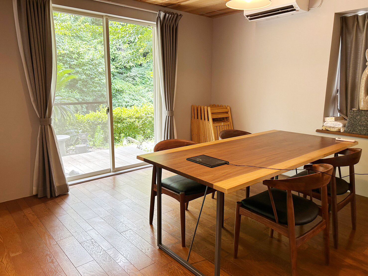 Een kamer met een houten tafel, vier stoelen, een schuifdeur naar een tuin en een radiator.