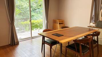 Een kamer met een houten tafel, vier stoelen, een schuifdeur naar een tuin en een radiator.