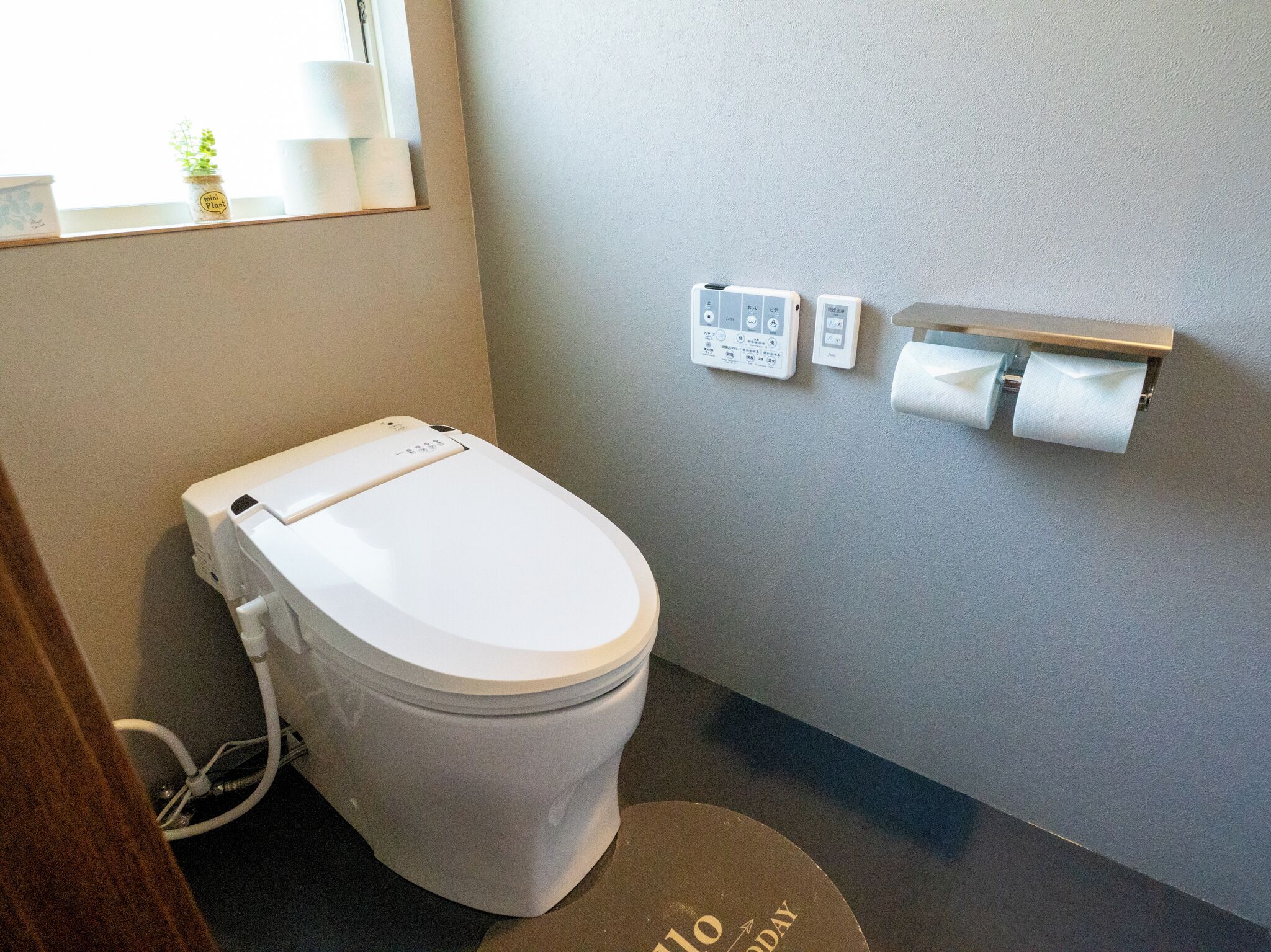 A modern toilet with a control panel, a toilet paper holder, and a small plant on the windowsill.