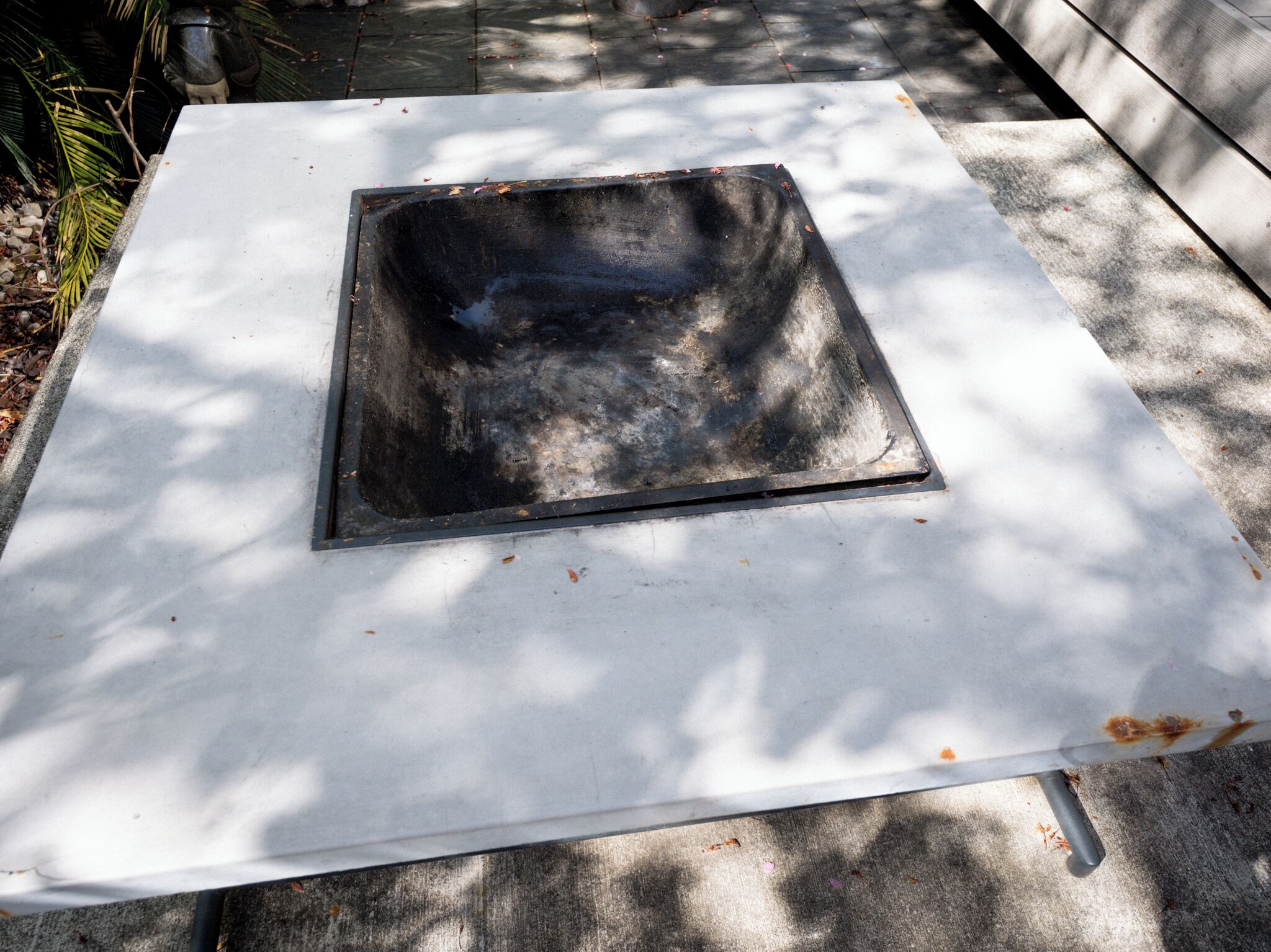 Une grille métallique carrée sur une surface blanche, entourée d’ombres et de quelques débris éparpillés.