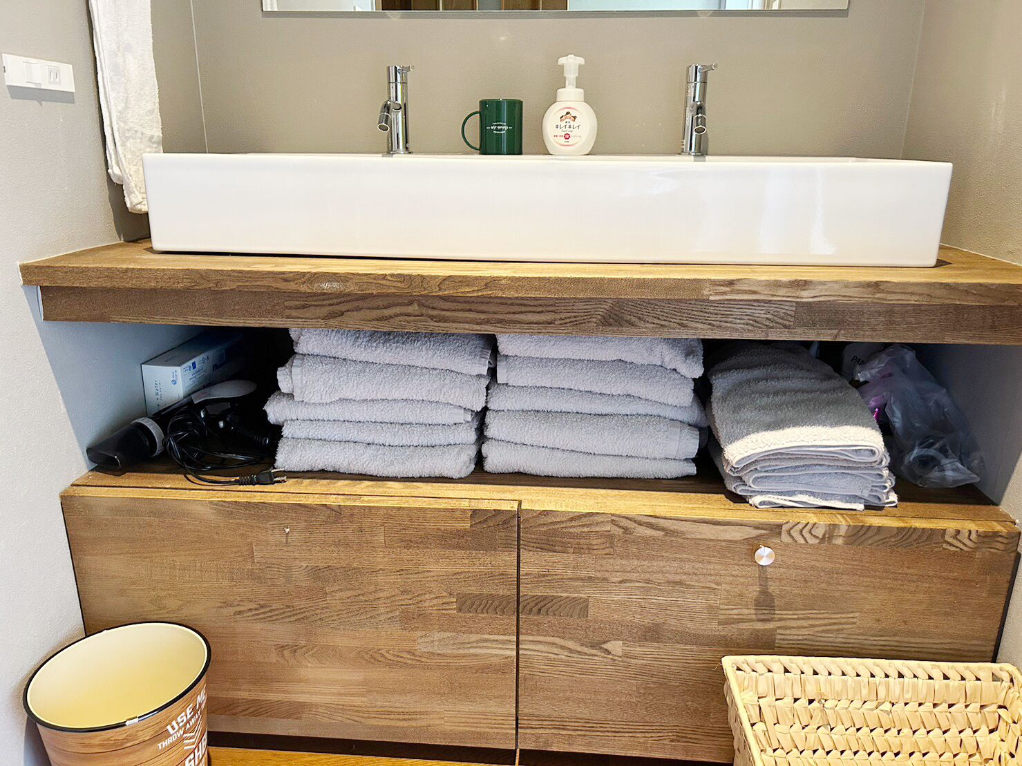 Un baño con tocador de madera, un lavamanos blanco y un espejo encima.