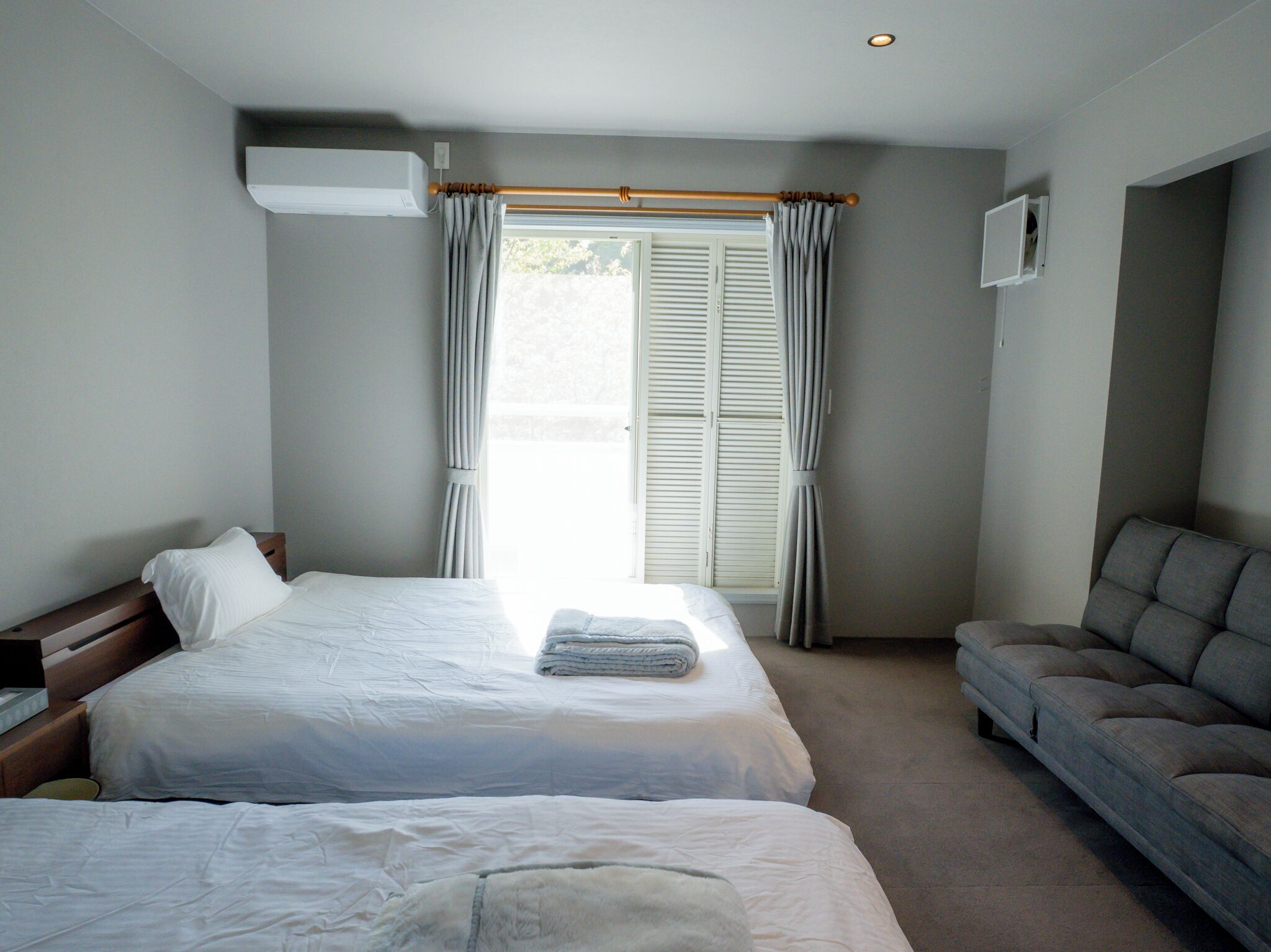 Quarto de hotel com duas camas, um sofá, uma janela com cortinas e um ar condicionado.