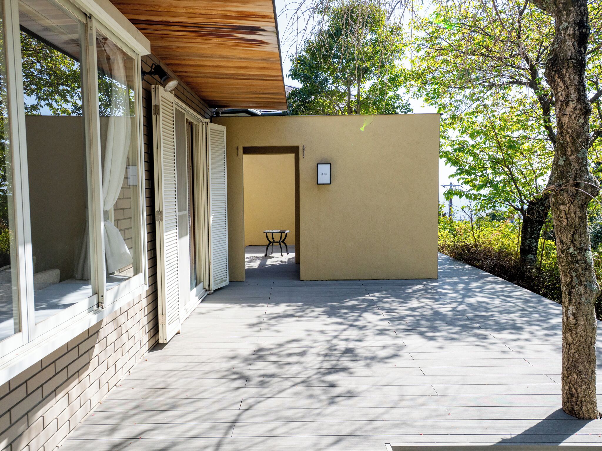 A modern building with a wooden deck, a small table, and a door leading to an interior space.