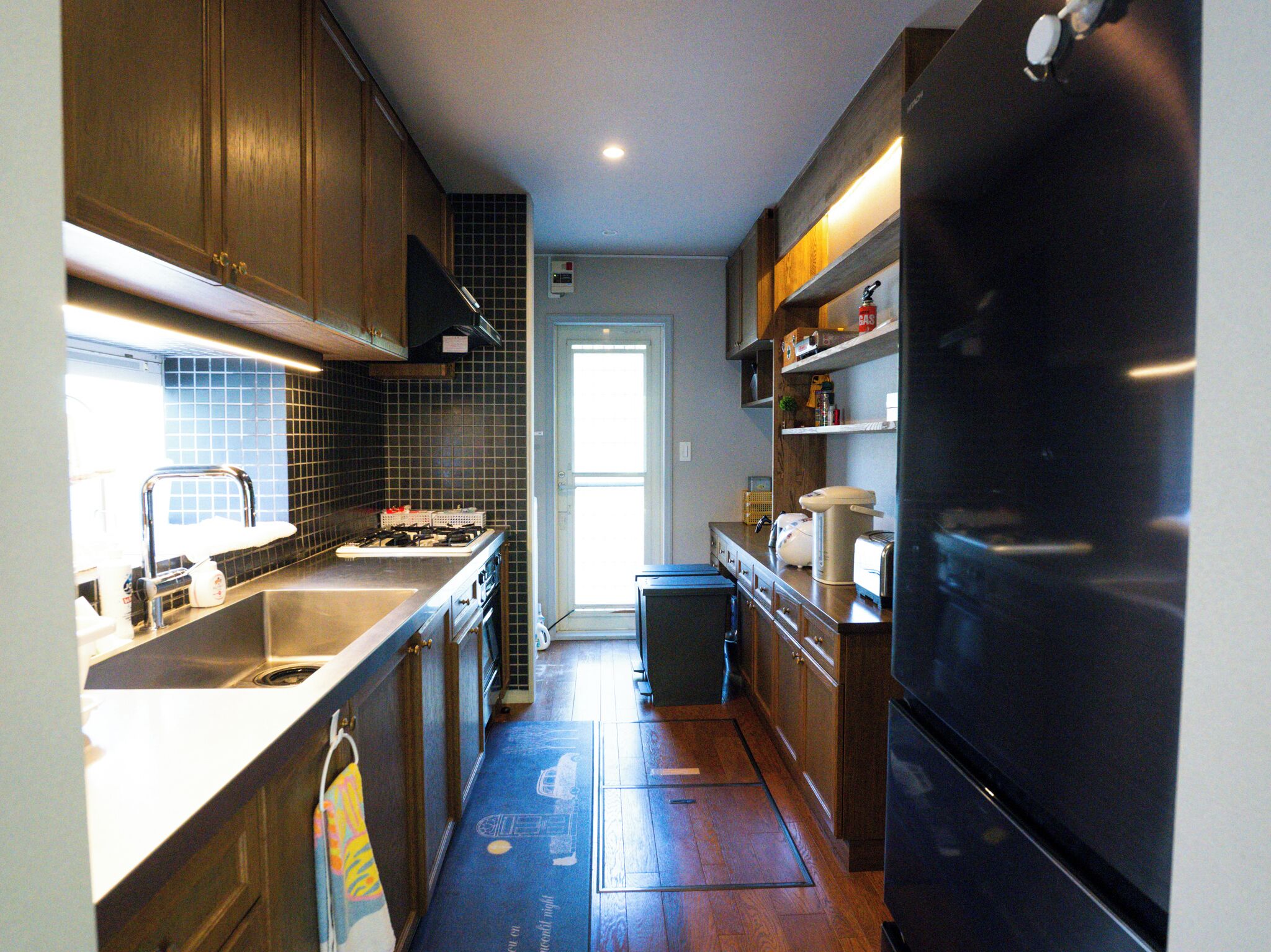 Una cocina con armarios de madera, un lavamanos de acero inoxidable, una estufa y un refrigerador negro.