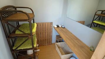 Una cama individual con estructura de madera y cojín de asiento tejido, un taburete pequeño de madera, una cesta tejida y un inodoro azul.