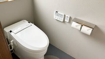 A modern bathroom with a white toilet, a wall-mounted bidet, and a toilet paper holder.