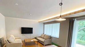 A modern living room with a wooden dining table, two sofas, a TV mounted on the wall, and a large window with curtains. - vacation inn  Izu Kogen (Ito)
