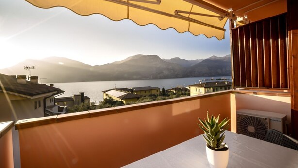 Ein Balkon mit Blick auf einen See und Berge, eine Topfpflanze und ein Tisch.