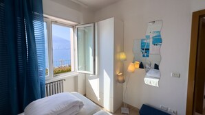 Ein Hotelzimmer mit Bett, Fenster mit Vorhängen, Stehlampe und einem an der Wand befestigten Spiegel.