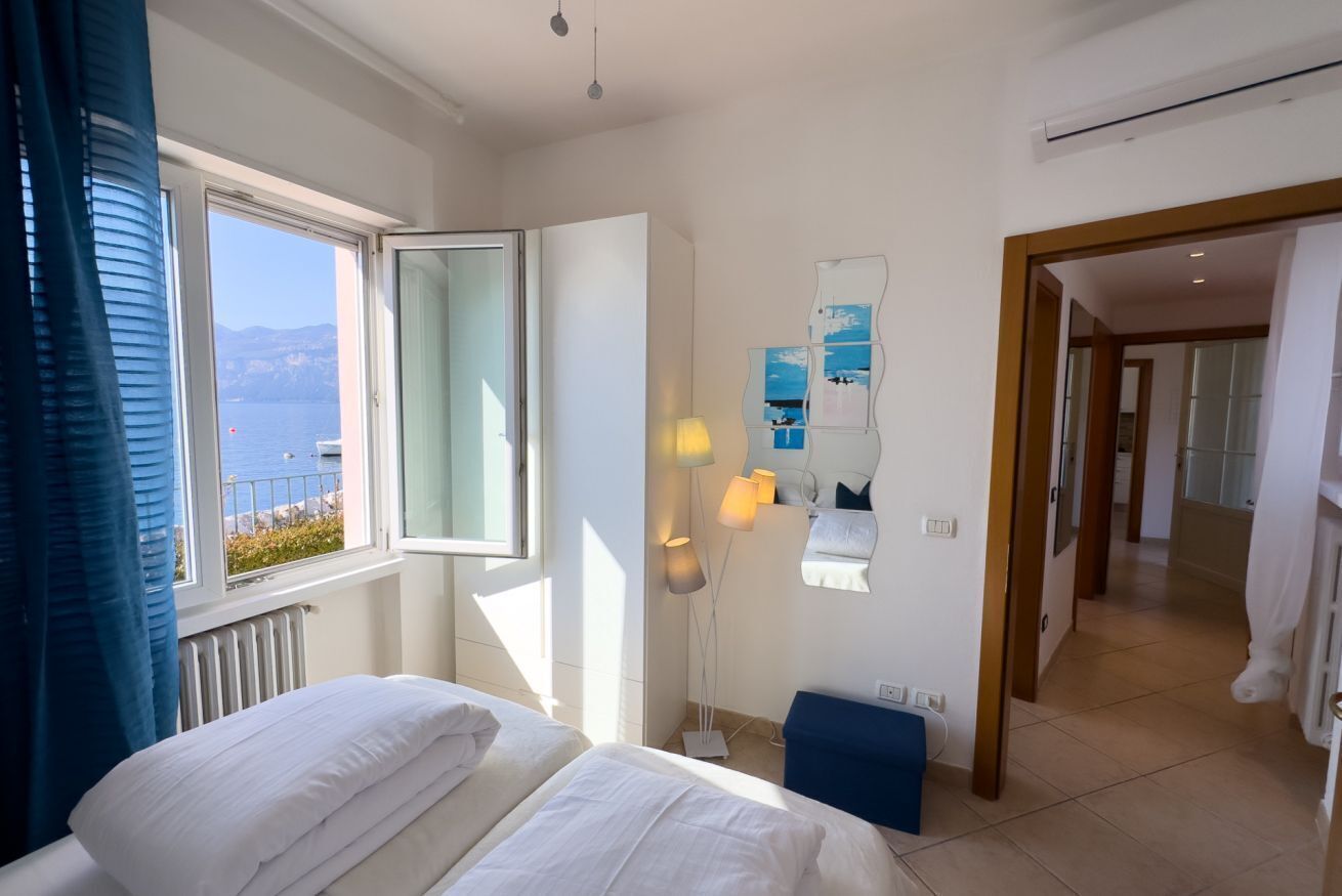 Une chambre d’hôtel avec un lit, une fenêtre donnant sur la mer, une lampe et un miroir.